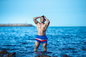 Bodybuilders are posing to show strength at the rocks by the sea.