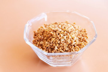 Glass bowl of roasted crushed peanuts isolated on table background.