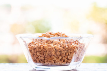 Glass bowl of roasted crushed peanuts with soft bokeh on background.