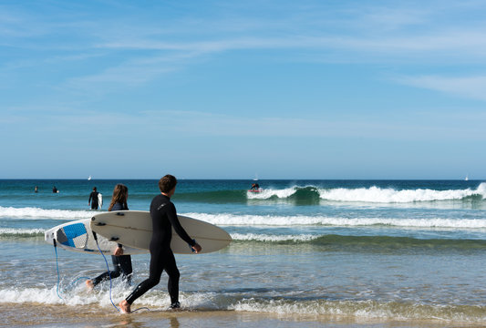 young surfers walking into the ocean and surfing on the west coast of Brittany in France at Toulinguet Beach near Camaret-Sur-Mer