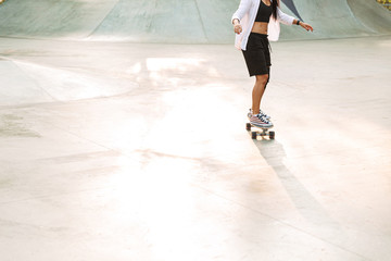 Cropped photo of energetic young woman riding skateboard in skate park