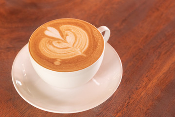 Coffee cup latte art in heart shape with a cup of dark coffee and dark chocolate on wooden table.Frothy drink for coffee break after working or weekend meeting