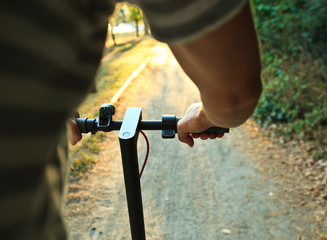 The young man is riding on the electric scooter through the evening city by the pathways