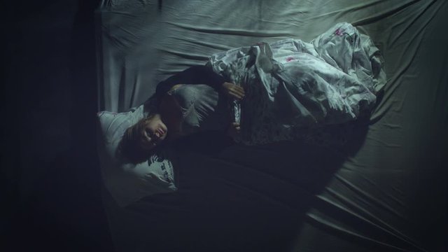 Sleeping woman. Restless sleep.  Top view. A woman sleeps on a bed. She flips from one side to the other.  Light headlamp from passing by the window cars fall on she.