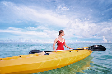 Young woman holding the sea kayak in the tropical calm lagoon.