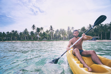 Young man paddling the sea kayak in the tropical calm lagoon.