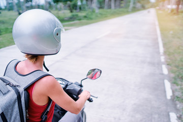 Fototapeta na wymiar Tropical travel and transport. Woman in helmet riding scooter on the road.