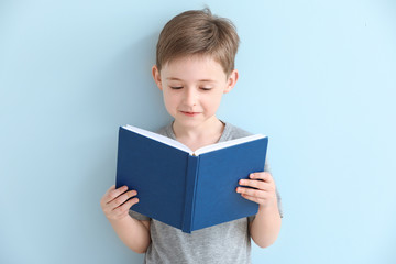 Little boy reading book on color background