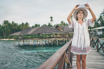 Vacation and technology. Outdoor portrait of pretty young woman taking photo with her smartphone on tropical beach.