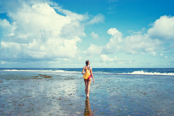 Tropical traveling. Young woman with waterproof backpack walking by low tide sea beach.