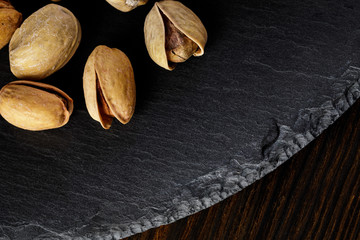 top view of salted pistachio nuts on stone board on wood background. copy space