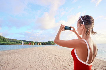 Travel lifestyle. Young woman taking photo of beautiful tropical beach on smartphone.