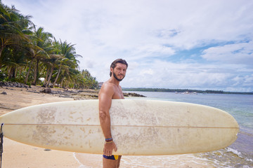 Hobby and vacation. Holiday on the beach. Young man carrying surf board.