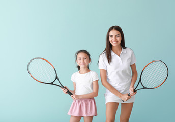 Little girl and her mother with tennis rackets on color background