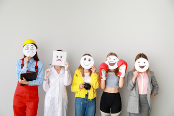 Group of female workers covering their faces with drawn emoticons against light background - obrazy, fototapety, plakaty