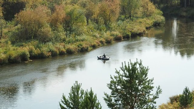 Autumn fishing on the river. A fisherman with a fishing rod on a rubber boat sails along the river