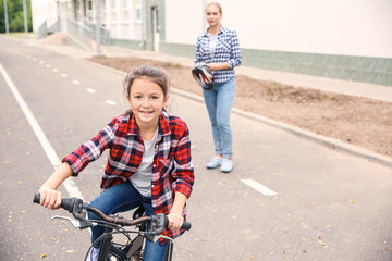 Obraz premium Mother watching after her little daughter who is riding bicycle outdoors