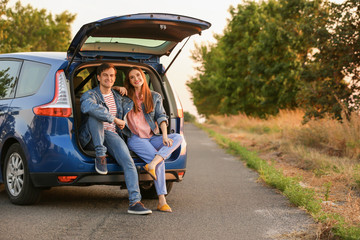 Happy couple sitting in trunk of their new car in countryside