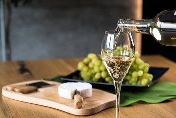 Pouring White wine with branches of grapes on a wooden table.