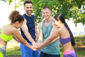 Group of young sporty people putting hands together outdoors