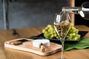 Pouring White wine with branches of grapes on a wooden table.