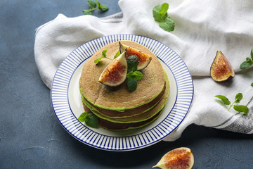 Plate with green pancakes and fig fruit on color background