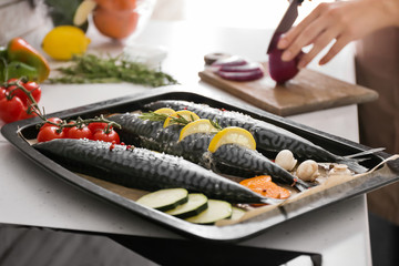 Tray with raw mackerel fish and vegetables on table in kitchen