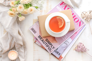 Cup of hot tea with book and magazines on white table