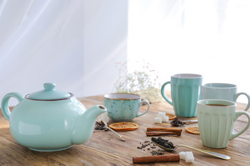 Cups and teapot with hot beverage on wooden table