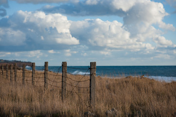 empty place near sea shore with barbed wire fence on border with blue sky and clouds on overcast sunset with copy space