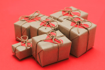 Romantic presents set. Gift boxes wrapped in brown craft paper and tie hemp string. Carton hearts. Red solid background. Delivered parcels.	