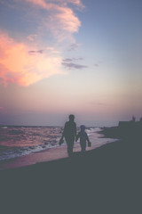 Fototapeta premium Mother and daughter walk along the beach at sunset