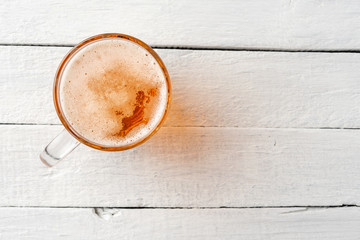 Cold beer mug with foam on white wooden table with copyspace. Close up