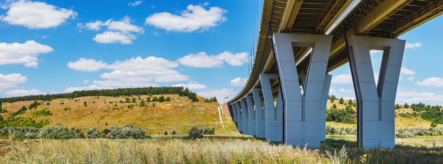 The panoramic view of the modern concrete car bridge above a green grassy field. Highway M4 