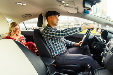 Photo of driver and blonde in back seat with phone in their hands sitting in taxi.