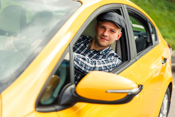 Photo of driver in plaid shirt sitting in yellow taxi on summer.