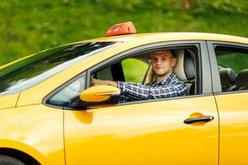 Photo of driver man in plaid shirt sitting in yellow taxi on summer.