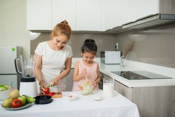 Obraz na płótnie Canvas Cute little girl and her mom in chef's hats are cutting vegetables cooking a salad and smiling