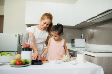 Obraz na płótnie Canvas Young Asian mother and daughter making freshly squeezed tomato smoothies, daughter is very happy
