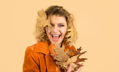 Fashionable woman in orange jacket with yellow oak leaves. Fashion autumn woman portrait. Fresh skin. Healthy smile. Girl with autumn leaf. Autumn beauty. Perfect woman fashion model with fall leaves.