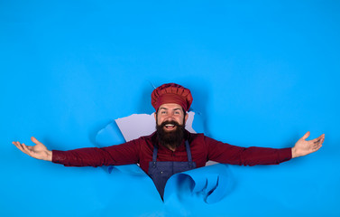 Professional happy man chef looking through paper hole. Male chef, cook or baker in hat and apron. Bearded man in chef uniform. Cooking, profession and business. Professional approach to business.