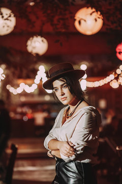 Fototapeta stylish beautiful girl in a hat on a background of lights in a cafe