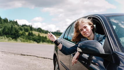 Happy woman travels by car in the mountains. Summer vacation concept. Woman out the window enjoying mountain view