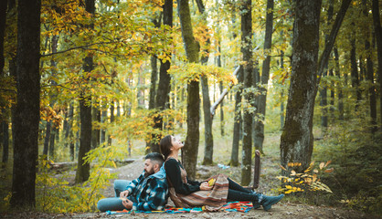 Young couple sitting outdoors at the park on beautiful autumn day. Laughing bearded man and pretty woman outside. Lifestyle, happy couple of two play on a sunny day in the park.