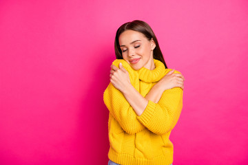 Obraz premium Portrait of cute girl embracing herself with closed eyes wearing yellow knitted sweater isolated over fuchsia background