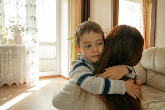 Mom hugs her son at home with light from the windows. Expression of family kindness and maternal love. Mutual understanding, sympathy and support of parents and children. Boy with joyful emotions.