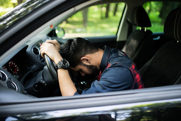 Closeup portrait tired young handsome man with short attention span, driving his car after long hours trip, trying to stay awake at wheel, isolated outside background. Sleep deprivation
