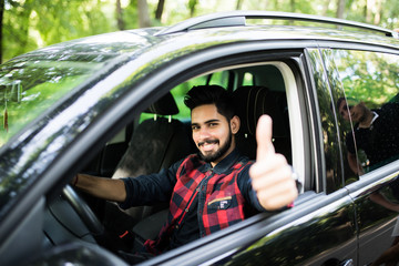 Attractive young indian man sitting in his car with thumb up smiling at the camera