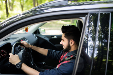 Portrait of an handsome smiling indian s man driving his car with white shirt