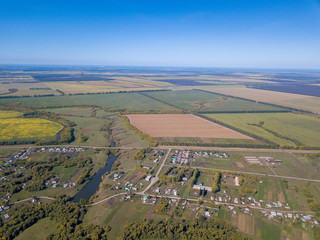 Drone aerial view of the village with pond at summer season. Roofs of the houses and farms between grass fields, trees and roads under clear blue sky. Penza region, Russia.Idyllic rural landscape.